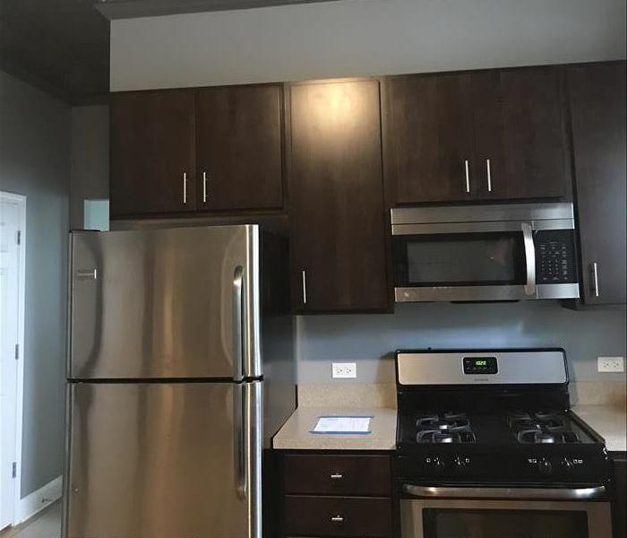 Clean new brown cabinets with a new stainless steel fridge and stove in a kitchen with white walls.
