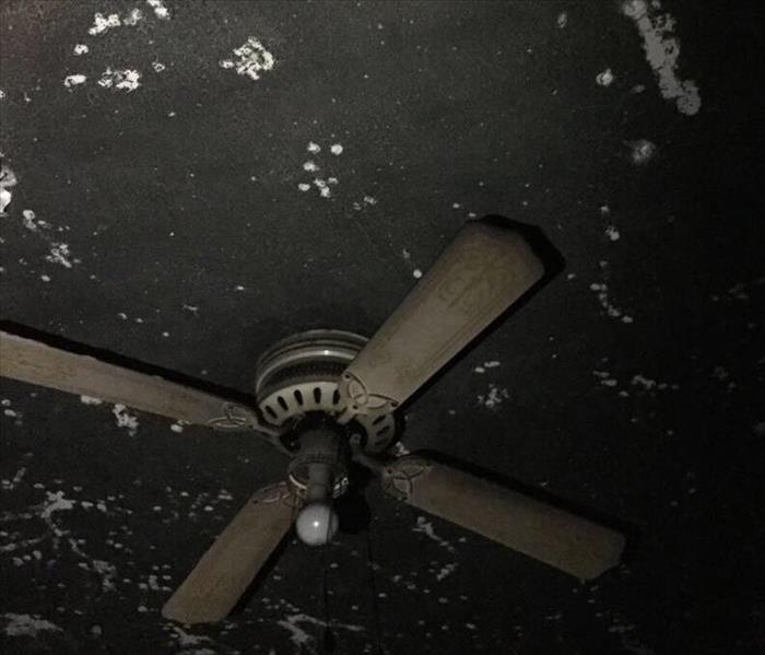 A white ceiling fan covered with black soot on a soot covered ceiling.