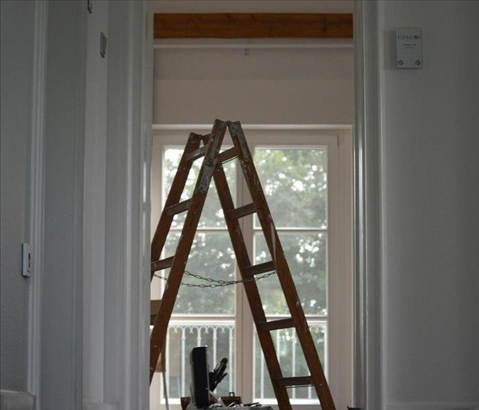 White bedroom with a brown ladder in front of a window.